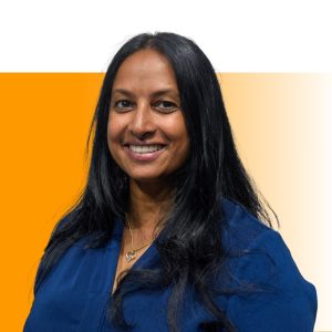 Professional headshot of a woman with long black hair wearing a blue shirt, smiling at camera against an orange and cream background