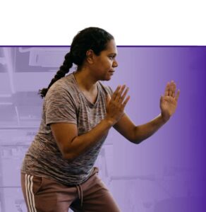 Woman in athletic stance during a boxing fitness class against purple background