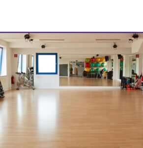 Spacious fitness studio with wooden floors, wall mirrors, training equipment, and colorful exercise balls ready for group fitness classes