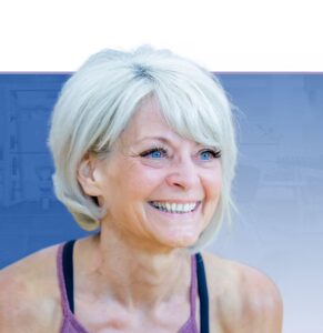Woman with white hair smiling at camera, wearing purple athletic top against blue background