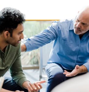 Older man in blue shirt mentoring younger man, demonstrating supportive coaching or counseling interaction