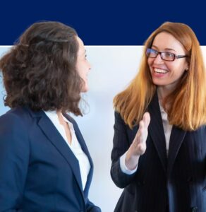 Two professional women in business suits having a friendly conversation and smiling