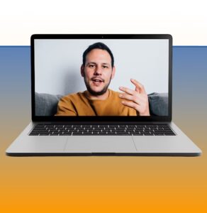 Man in yellow shirt on laptop video call, gesturing while speaking to camera