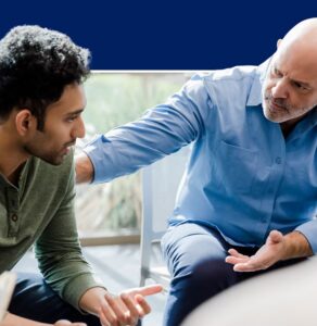 Older man in blue shirt placing supportive hand on younger man's shoulder during a mentoring or coaching conversation