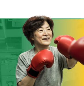 Woman smiling while wearing red boxing gloves in a boxing stance against a green and yellow background