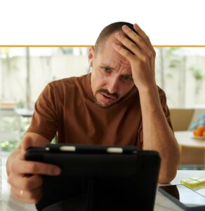 Man looking stressed while holding a tablet, hand on forehead, illustrating workplace stress or mental health concerns