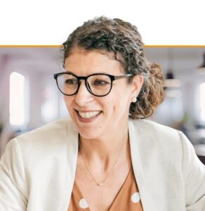 Woman wearing glasses and tan blazer smiling in modern office setting