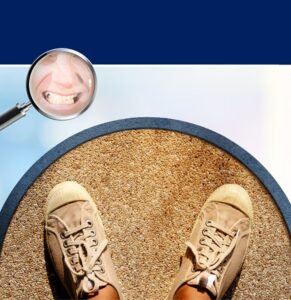 Person standing on sandy ground wearing hiking boots with magnifying glass showing smiling face reflection above
