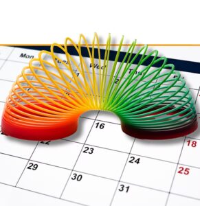 Colorful coiled spring toy showing gradient from red to green positioned on a calendar, symbolizing scheduling and time management for wellness programs