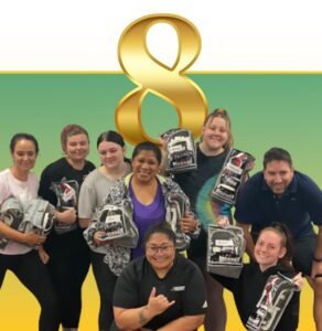 Team of 9 people holding DISC profile cards, standing under a large gold ampersand symbol against green and yellow background