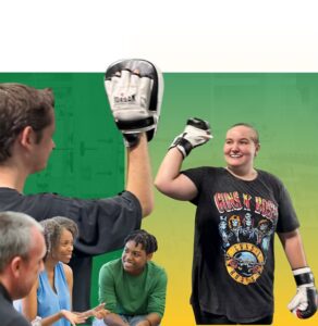 Woman in boxing gloves high-fives an instructor while smiling during a group fitness class with participants watching