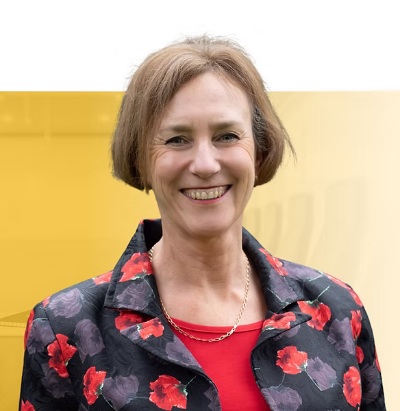 Smiling woman with shoulder-length brown hair wearing a red top and black floral jacket, portrait photo against yellow background