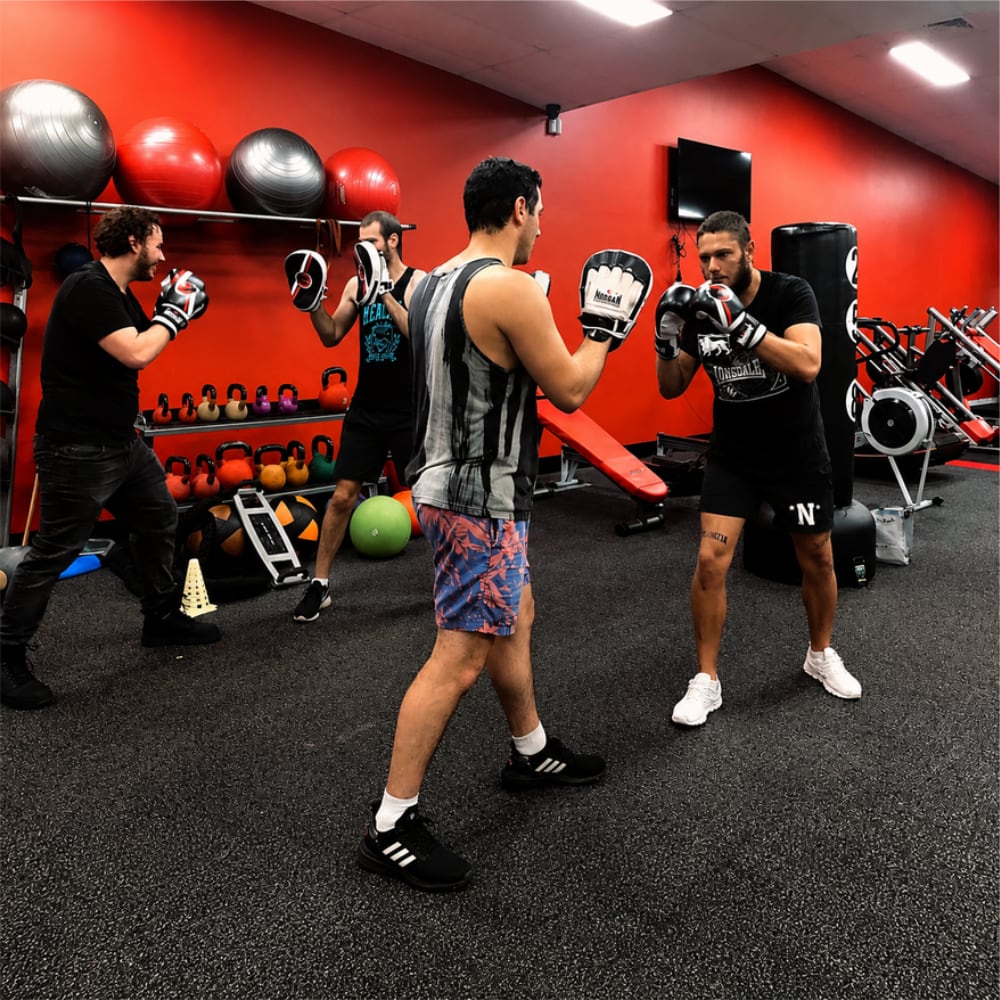 Boxing trainer coaching client in boxing gloves during fitness class at modern gym with red walls and equipment